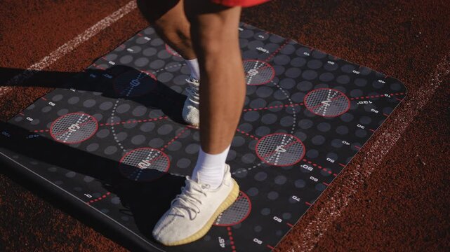 Close-up. Legs of an unrecognizable male athlete in white running sneakers during a workout on the platform P9. A man performs exercises while standing on a fitness mat for 3D training on a stadium