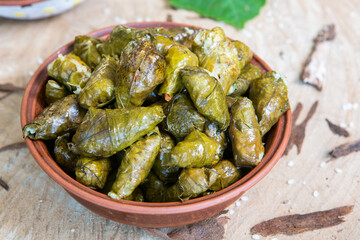 Dolma a stuffed grape leaves in a clay bowl on wooden background