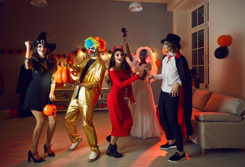 Overjoyed diverse friends in horror costumes have fun celebrate fall at Halloween party in...