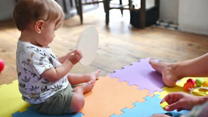 Caucasian cute baby in patterned shirt and green shorts playing with colorful educational toys outdoors on sunny day.