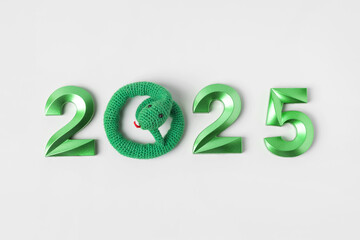 Knitted toy green snake and green numbers. The symbol of the year 2025 on a gray background.