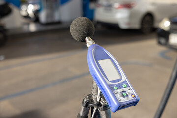 A sound level meter with a screen and buttons is on a tripod in petroleum fuel station.