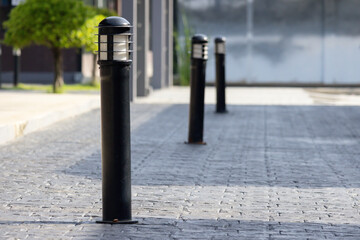 A black pole with a light on top stands in front of a building. light steel bollard on footpath.