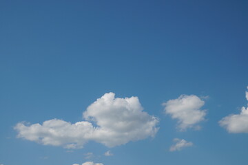 White fluffy clouds in the sky. Blue sky and cloud cover on a sunny summer day. Empty background, copy space