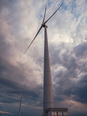 Bottom view of a tall wind turbine silhouette against dramatic sunset sky.