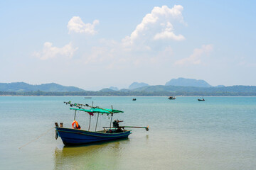 A small fishing boat that fishermen take out to catch fish during the day, with a beautiful mountain range in the background at Koh Phithak, Thailand.
