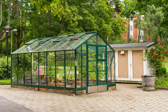 Beautiful greenhouse glass house in the garden yard near the villa. There are lots of pots with blooming blossom colorful flowers. Landscape garden design. Greenhouse for growing plant seedlings.