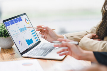 Two professional analyzing financial data graphs, charts on laptop display at a modern workspace. Financial analysis or business evaluation conceptT