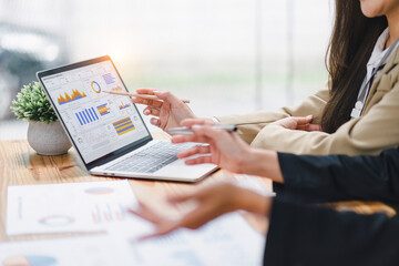 Two professional analyzing financial data graphs, charts on laptop display at a modern workspace. Financial analysis or business evaluation concept
