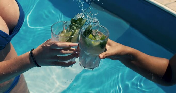 Super slow motion of happy couple in love clinking with cool alcohol cocktails to celebrate start of their honey moon vacation at poolside bar of luxury hotel resort at summer holidays, 1000 fps.