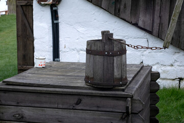 old wooden bucket of water hanging over the well with a wooden building