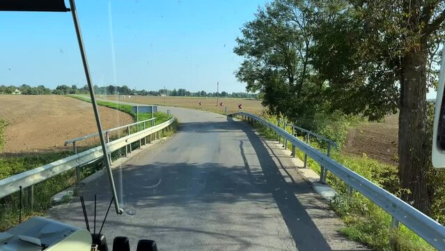 Dirty bus windscreen view driving through agricultural land on a sunny summer day in Lithuania.
