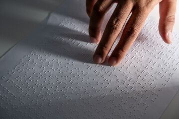 Hand of a blind person reading some braille text on page paper to learn. Finger of blind student...
