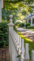 A white picket fence lines a manicured green hedge, creating a beautiful border between a private property and the public sidewalk