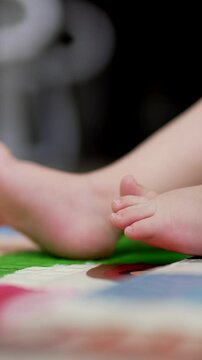 Caucasian child lies on back bent in knees. Close up of tiny baby feet moving slowly. Blurred backdrop. Vertical video