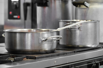 Close up view of casseroles at a commercial kitchen. Preparing and cooking food in a commercial kitchen. Unrecognizable Chefs in the background. High quality photography