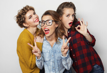 Three cheerful and happy young female friends laughing on gray background