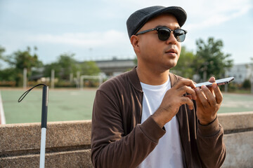 Young asian blind man using application on mobile phone to helping accessibility for persons with visual impairment. Technology for blind people sending voice message or navigation.