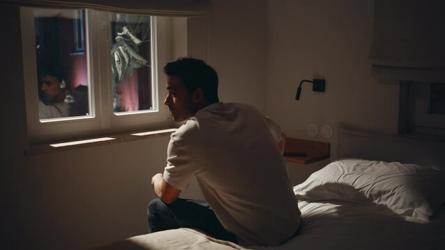 Exhausted guy suffering insomnia at dark bedroom. Depressed man sitting home bed
