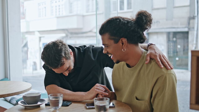 Happy same-sex couple hugging sitting coffee shop close up. Men laughing at date