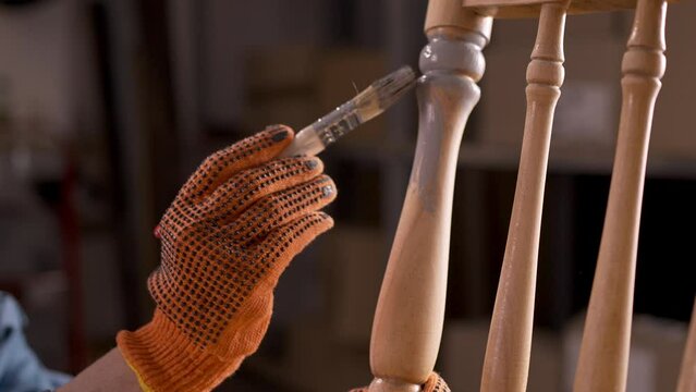 Close-up of female hands with painting brush upcycling furniture In workshop at home painting old wooden chair