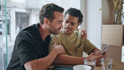 Same sex lovers smiling looking mobile phone screen sitting coffee shop close up
