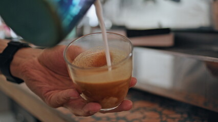 Barista hands preparing cappuccino in cafeteria with espresso machine close up.
