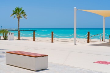 Beach shade tent with modern wooden bench on seashore. Beautiful landscape of white sandy beach with clear turquoise water in Saadiyat island, United Arab Emirates