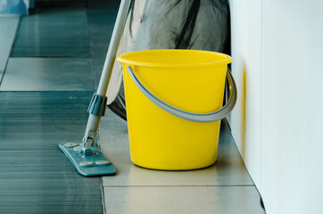 There is yellow bucket and mop on floor, tools for cleaning premises © Ninaveter