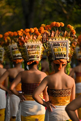 A group of women wearing orange headdresses and white skirts are standing in a line. The women are dressed in traditional clothing and appear to be part of a cultural event