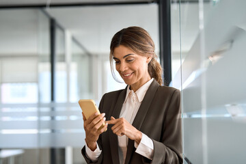 Smiling mature professional manager entrepreneur using smartphone standing in office at work. Happy...