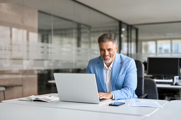 Happy senior 50 years old professional business man wearing suit using computer sitting at desk. Busy smiling middle aged businessman executive investor bank manager working on computer in office.