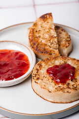 Hot Toasted Crumpets with piece of butter on a plate with strawberry jam. Perfect tasty breakfast popular in England, UK
