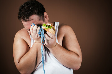 Funny fat man on a diet eating a burger. Brown background.