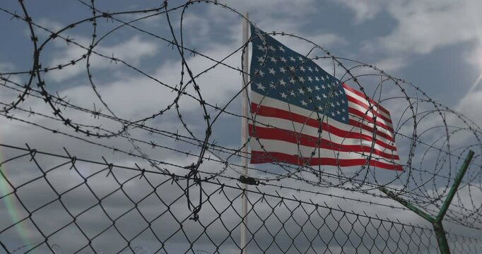 USA waving flag on country border concept. American blowing banner with barbed wire fence.