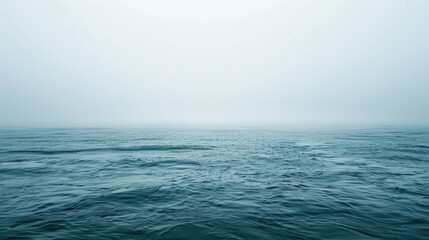 Obraz premium A vast expanse of ocean under a foggy sky can be seen. The water is calm but exhibits slight ripples, and the horizon is barely visible through the mist.