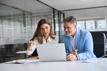 Two busy happy middle aged professional business man and woman executive leaders team using laptop...