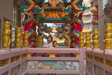Portrait of Asian middle-aged mother and daughter together in a Chinese temple, with funny pose happy time, perspective view, child at 9 to 10 years old, landscape image.