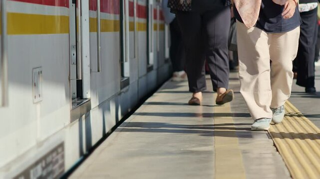 Passengers' feet are walking on the edge of the tracks with a commuterline electric train car stopped beside it during rush hour.