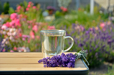 napój w szklance na stole obok bukietu lawendy, napój z lawendą w przeźroczystej szklance, herbata ziołowa z lawendą na stole obok kwiatów lawendy, stolik bambusowy, herbal tea with lavender © kateej
