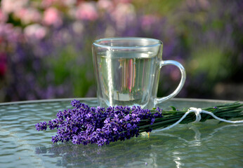 napój z lawendy w szkalnce na stoliku ogrodowym, lawenda na stole obok szklnki,lavender drink in glass and lavender flowers, drink with lavender and lavender flowers on glass coffee table