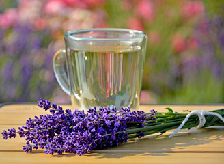 napój w szklance na stole obok bukietu lawendy, napój z lawendą w przeźroczystej szklance, herbata ziołowa z lawendą na stole obok kwiatów lawendy, stolik bambusowy, herbal tea with lavender © kateej