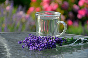 napój z lawendy w szkalnce na stoliku ogrodowym, lawenda na stole obok szklnki,lavender drink in glass and lavender flowers, drink with lavender and lavender flowers on glass coffee table