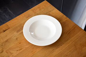 Ceramic white flat plate for food on wooden table top view