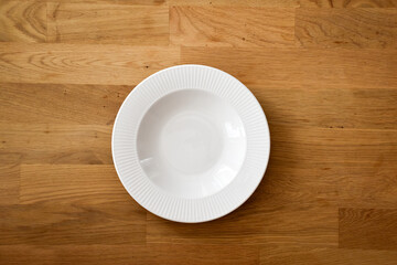 Ceramic white flat plate for food on wooden table top view