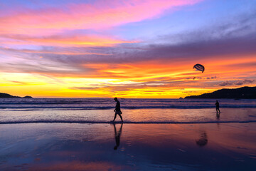 Fototapeta premium Silhouette of parasailing and people on the beach with the Most beautiful and colourful sunset on Patong Beach Phuket Island Thailand