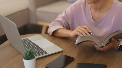 Female entrepreneur working at home to reading a book and searching business data on laptop