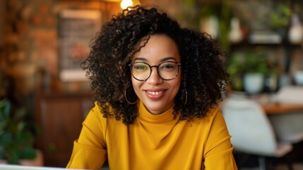 Fototapeta premium Smiling Woman with Curly Hair, Wearing Glasses and a Yellow Sweater, in a Cozy Office Setting