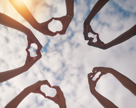 Sky, heart and hands of people together for community, collaboration and teamwork outdoors. Diversity, solidarity and low angle of group with gesture, emoji and symbol for love, charity and support