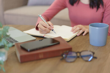 Young businesswoman writing down idea about new startup project in notebook while working at home © Pichsakul